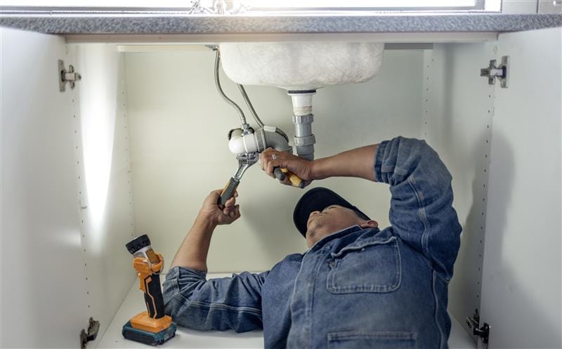 Plumber repairing pipes beneath a bathroom sink in Daytona Beach