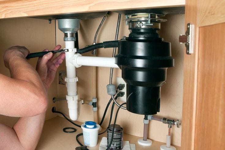 Plumber installing a garbage disposal beneath a kitchen sink in Daytona Beach