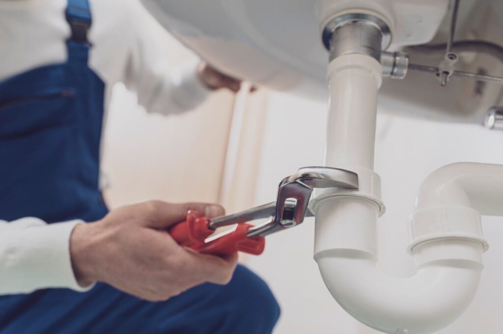 Plumber repairing a white drain pipe beneath a sink in Daytona Beach